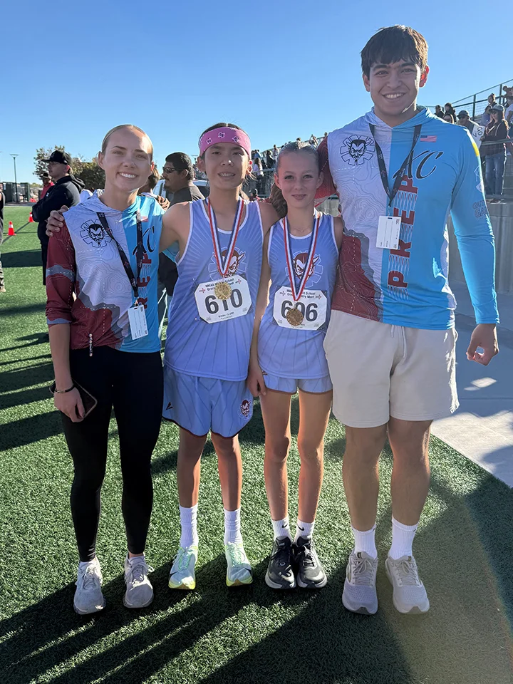 Two student runners wearing medals pose with two coaches